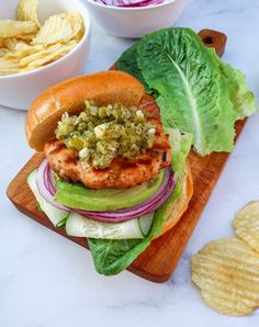 a sandwich with lettuce, tomato and other toppings sits on a cutting board next to chips