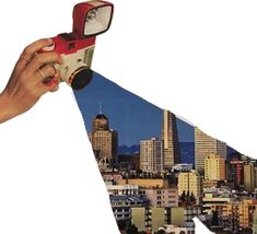 a hand holding a red and white camera over a city