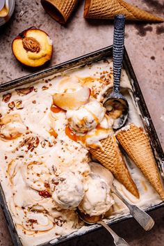 two scoops of ice cream with peaches and pecans on the side in a metal pan