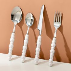 three forks, two spoons and one knife are lined up against a wall with beads