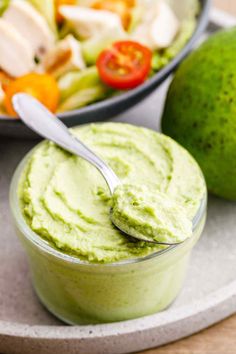 a bowl of guacamole with a spoon in it next to a salad