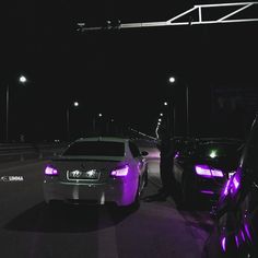 two cars are parked on the side of the road at night with purple lights around them