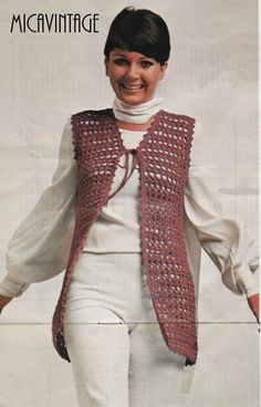 a woman wearing white pants and a crocheted vest is smiling at the camera