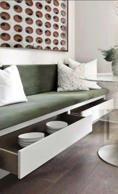 a green couch with white pillows and plates on the bottom shelf in a living room