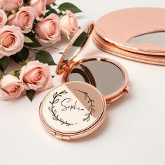 the compact mirror is next to pink roses and a gold case with writing on it