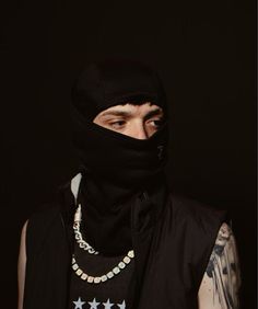 a man wearing a black hood and bandana with stars on his chest is looking at the camera