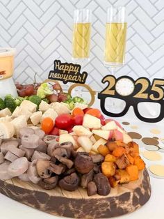 a wooden platter filled with different types of food and glasses next to a happy new year sign