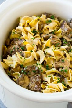 a white bowl filled with pasta and meat covered in parsley on top of a table