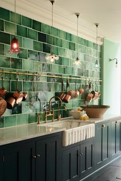 a kitchen with green tiles on the wall and copper pots hanging over the sink in front of it