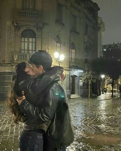 a man and woman are kissing in the rain on a cobblestone street at night