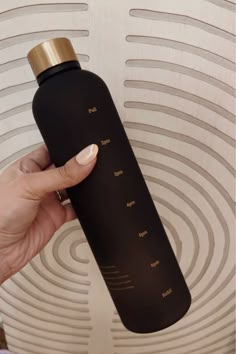 a person holding a black and gold bottle in their left hand with the lid up