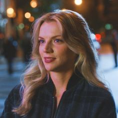 a woman with long blonde hair standing on the side walk at night, looking off into the distance