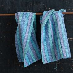 two blue and white striped towels hanging on a clothes line with a wooden pole in the background