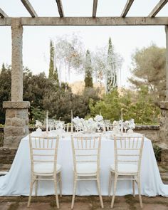 the table is set with white linens and flowers on it, along with candles