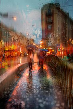 two people walking down the street in the rain with umbrellas over their heads and buildings behind them