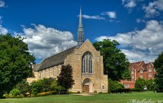 an old church with a steeple surrounded by trees and flowers on a sunny day