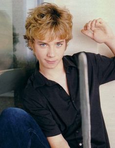 a young man sitting on the ground with his arm up and looking at the camera