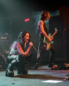 a woman kneeling down on the ground with a microphone in her hand and two men standing behind her