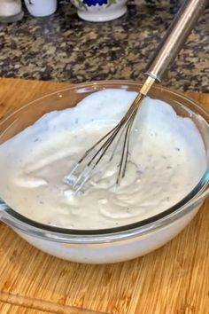 a whisk in a glass bowl on top of a wooden cutting board