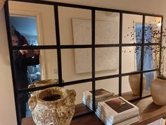 a table with vases and books on it in front of a mirror that is reflecting the room