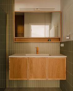 a bathroom with green tile and wooden cabinetry, mirror above the sink is an orange soap dispenser