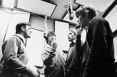 black and white photograph of four men in a radio studio talking to one another while the man is holding a microphone