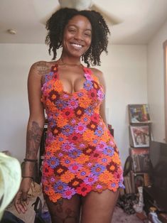 a woman in a crochet swimsuit smiling and standing next to a bed