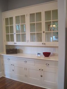 an empty kitchen with white cabinets and wood flooring, along with a red bowl on the counter