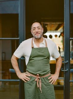 a man wearing an apron and glasses standing in front of a door with his hands on his hips