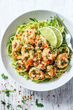 a white bowl filled with pasta and shrimp on top of a wooden table next to a fork