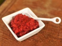 a small white bowl filled with red stuff on top of a wooden table next to a bottle