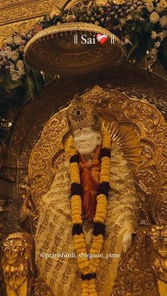 the statue is in front of an ornate gold background with flowers and garlands on it