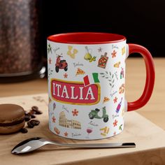 a red and white coffee mug sitting on top of a wooden table next to a cookie