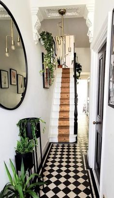 a hallway with black and white checkered flooring, potted plants and mirrors