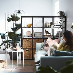 a woman sitting on a couch reading a book next to a plant in a living room