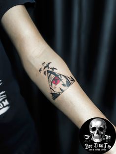 a man's arm with a skull and red eye tattoo on the left forearm