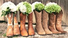 four pairs of cowboy boots with flowers in them are lined up against a wooden fence