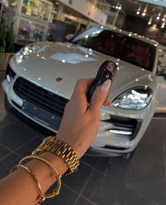 a hand holding a remote control in front of a car at a showroom with other cars