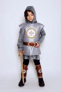 a little boy dressed up in a knight costume and holding a wooden stick while standing against a white background