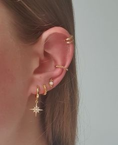 a close up of a person wearing gold ear cuffs with stars and pearls on them