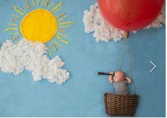 a baby in a basket with a balloon and clouds painted on the wall behind it