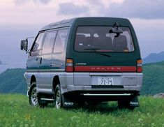 a van parked on top of a lush green hillside next to the ocean with mountains in the background