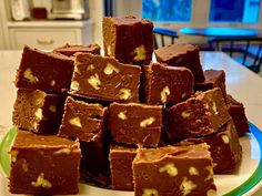 a pile of brownies sitting on top of a green and white plate next to a window