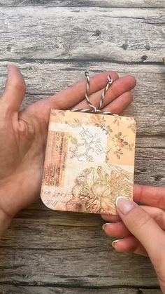 two hands holding a small piece of paper on top of a wooden table next to scissors