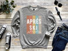 Stay cozy and stylish this winter with our Retro Apres Ski Mountain Sweatshirt. Featuring a vintage design, mountains and the words "Après Ski," this sweatshirt is the perfect addition to your winter wardrobe. Made with quality, soft and comfortable material, this sweatshirt is perfect for those chilly days on the slopes or relaxing by the fire. Whether you're hitting the slopes or enjoying après ski, this sweatshirt is sure to become a go-to favorite. Order yours today and get ready to conquer the mountains in style.  This crewneck sweatshirt fits comfortably and is great for warm weather as wel. The side seams are also stitched to prevent irritation. Features - Air jet yarn for softer feel and reduced pilling - Loose fit - Tear away label Care Instructions - Wash in warm water, max 40C o Winter Long Sleeve T-shirt For Outdoor Activities, Winter Outdoor Long Sleeve T-shirt, Winter Casual T-shirt For Outdoor Activities, Casual Winter T-shirt For Outdoor Activities, Winter Crew Neck T-shirt For Outdoor, Retro Winter T-shirt With Graphic Print, Sporty Sweatshirt With Graphic Print For Outdoors, Winter Outdoor T-shirt With Relaxed Fit, Sporty Sweatshirt With Graphic Print For Outdoor Activities