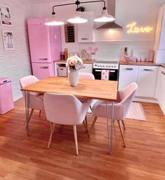 a pink kitchen with white appliances and wooden table in the center, surrounded by light colored chairs