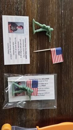 two toy army men and an american flag on a wooden table next to some stickers