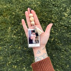 a hand holding a small photo with a tassel hanging from it's thumb