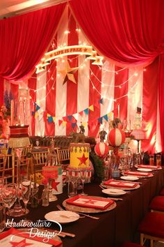 a table set up for a party with red drapes and decorations on the walls