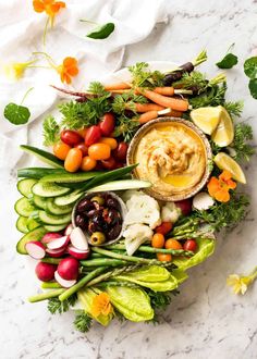 an arrangement of vegetables and dip in a bowl on a marble countertop with flowers